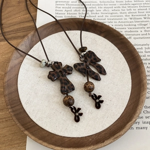Détail des pendentifs croix et nœud à imprimé léopard sur des colliers marrons style vintage
