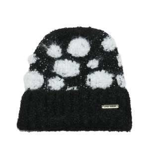Detailed close-up of a black knit beanie with white polka dots and a gold metal logo tag