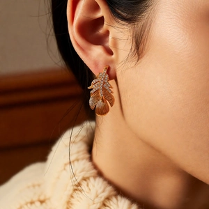 Detailed view of 18k gold plated feather earrings with clear stones on a model