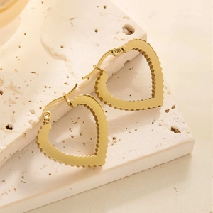 Détail des boucles d'oreilles créoles cœur dorées polies sur une surface en pierre