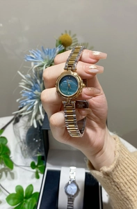 Detail of teal mother-of-pearl watch face with golden floral bezel and steel strap
