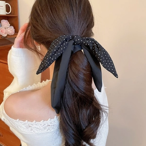 Detail of a black polka dot bow scrunchie with long ribbons on a ponytail style
