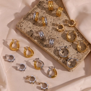 Flat lay of multiple gold and silver C-shaped earrings on elegant silk and stone textures