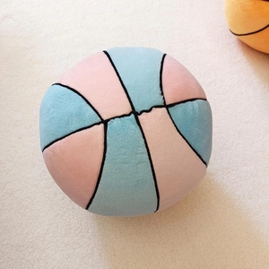 Soft basketball-shaped plush pillow in pastel pink and blue on a cozy white rug