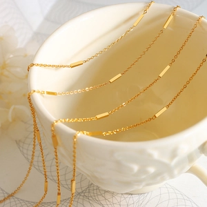 Minimalist gold plated necklace with rectangular bar links on a white ceramic cup