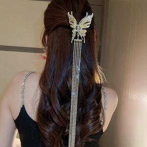 Détail de pince à cheveux papillon dorée avec de longues chaînes à pompons strass