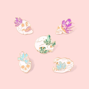 Detail view of five skull and crystal enamel pins in soft pastel macaron colors