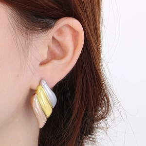 Detail of three-tone 18K gold plated wing-shaped stud earrings worn on ear