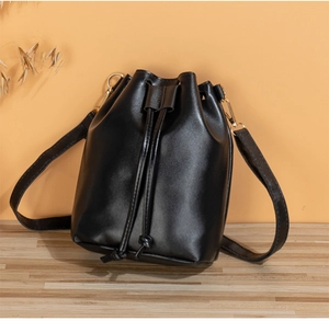 Detail of a black drawstring bucket bag with gold hardware on a light wood surface