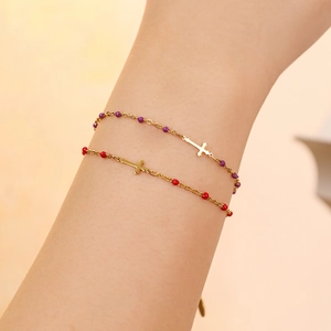Detail of stacked gold cross bracelets with purple and red enamel beads on wrist