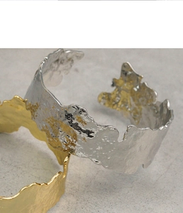Détail de bracelets métalliques dorés et argentés avec texture de lave sur fond de pierre