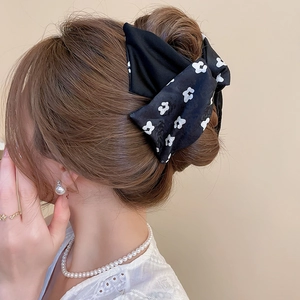 Close-up of a large black floral bow hair clip worn elegantly on a messy bun hairstyle