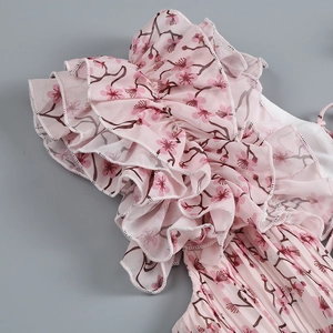 Détail d'une robe en mousseline rose fleurie avec volants étagés et texture plissée