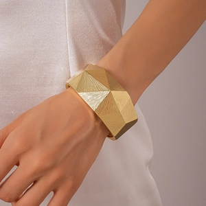 Detail of wide geometric faceted gold cuff bracelet with textured metallic surface