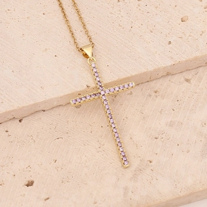 Golden cross necklace with pink gemstones on beige stone background for a stylish look