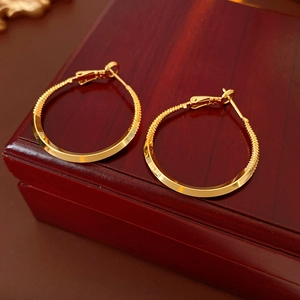 Detailed view of golden twisted hoop earrings on a vintage wooden jewelry box surface