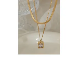 Macro detail of gold layered necklace featuring flat snake chain and square zircon pendant