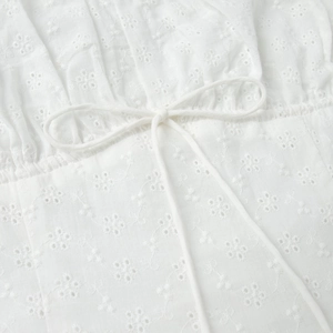 Λεπτομερής προβολή του λευκού κεντήματος eyelet και των κορδονιών στο βαμβακερό φόρεμα