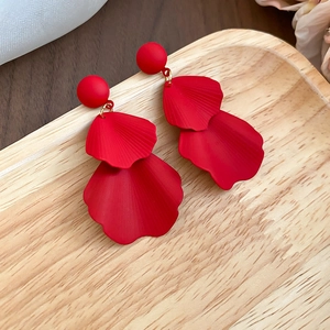 Detailed macro of red matte petal earrings with gold links on a wooden tray