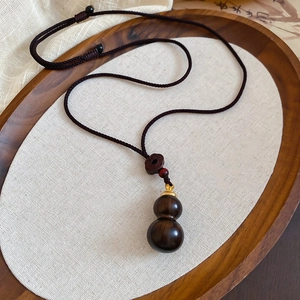 Macro shot of dark wood gourd pendant with braided cord in a minimalist Zen tray