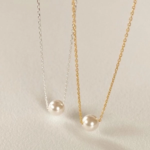 Detailed comparison of gold and silver pearl pendant necklaces on a cream background