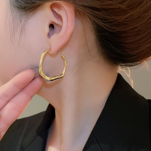 Close-up of a minimalist irregular golden hoop earring with organic fluid lines on a model
