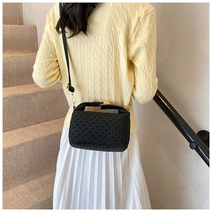 Detail of black woven shoulder bag with gold hardware and removable strap on model