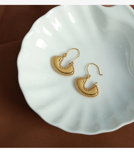 Detailed macro view of gold-plated fan-shaped earrings with bead edges on a shell tray