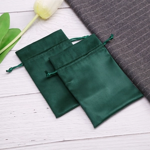Detail view of two dark green velvet drawstring jewelry pouches on white wood background