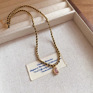 Detailed macro of a black and gold braided chain necklace with a pink zircon pendant