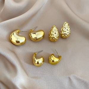 Detail view of gold geometric stud earring set on champagne silk fabric background