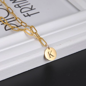 Close-up of golden paperclip chain necklace with a round letter K pendant detail