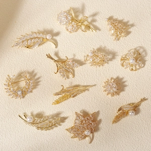 Elegant gold zircon brooches in floral and wheat designs with pearls on beige background