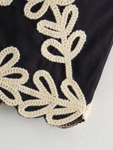 Détail de la broderie florale crème sur tissu noir avec finitions de haute qualité