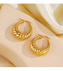 Détail macro de boucles d'oreilles torsadées en plaqué or 18K sur un support en pierre