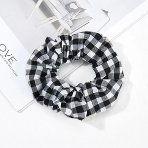 Détail d'un chouchou en tissu à carreaux noir et blanc sur fond blanc minimaliste