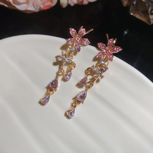 Detail of gold flower earrings with pink and purple tassels on a shell tray
