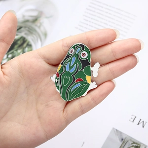 Macro shot of green cartoon enamel pin held in hand to show size and alloy texture