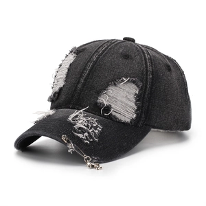 Detail of distressed black denim baseball cap with silver safety pin and cross pendant