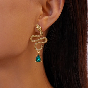 Close-up of golden snake earrings with emerald green teardrop crystals on a model