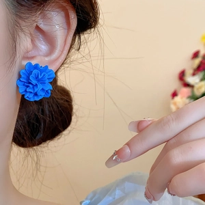 Détail de boucles d'oreilles fleur en résine bleue portées par un mannequin en intérieur