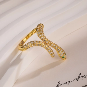 Detail of a gold snake ring with white and green zircons next to a lifestyle card