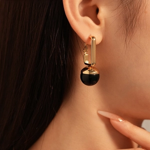 Close-up of golden rectangular hoop earrings with black resin round bead pendants on model