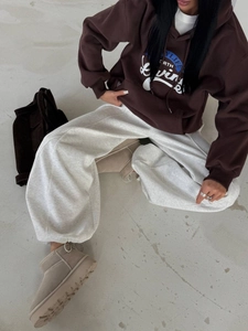 Dettaglio felpa con cappuccio marrone oversize con stampa blu e pantaloni sportivi grigi