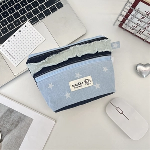 Detailansicht einer blauen Denim-Kosmetiktasche mit Sternenmuster und Fransenrand.