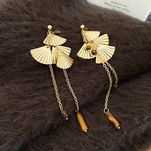 Detailed macro of golden fan-shaped tassel earrings with tiger eye beads and metal fringe