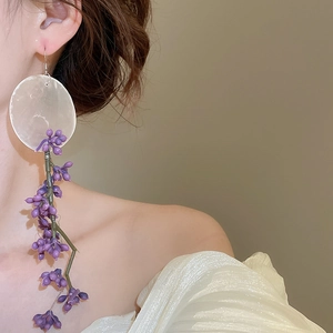 Detailed view of long asymmetric purple floral tassel earrings worn by a model