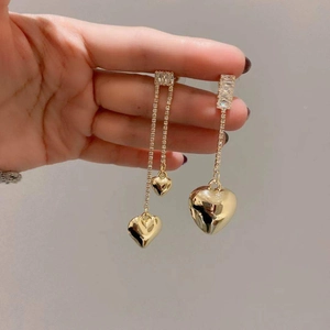 Macro detail of asymmetric gold heart earrings with dangling rhinestone fringe and chains