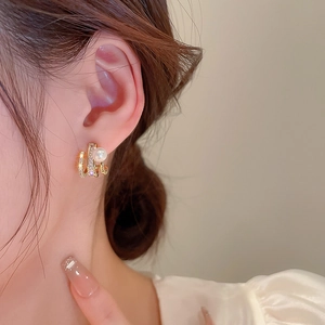 Close-up of golden claw earrings with pearls and zircons worn on model's ear