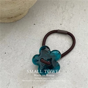 Close-up of a blue acrylic flower elastic hair tie on a minimalist grey stone surface